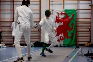 Students fencing during practice session with Welsh flag in background