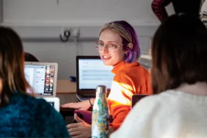ENU student in orange sweater working on digital project with classmates