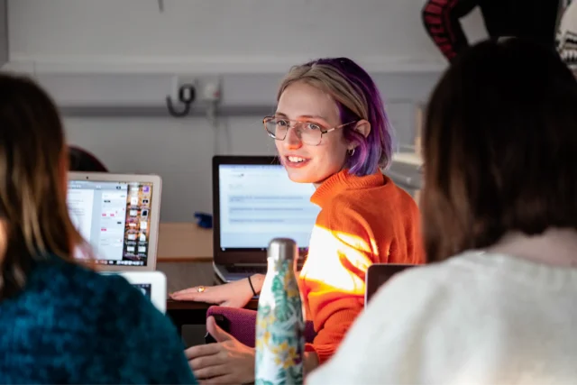 ENU student in orange sweater working on digital project with classmates