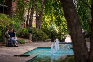 UoL campus with water feature and students sat on bench talking