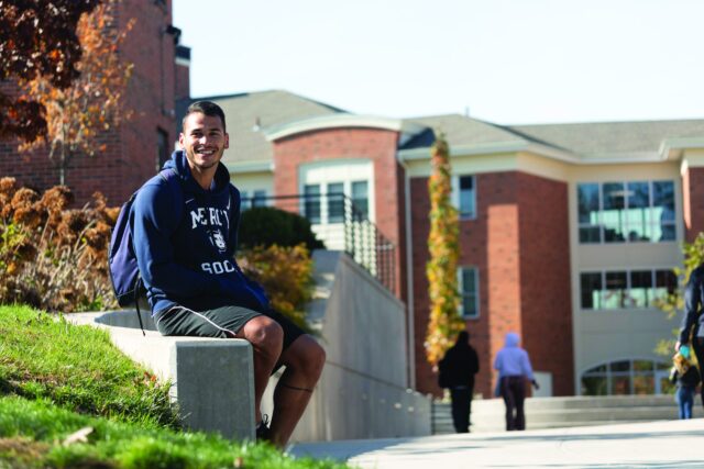 Mercy student sat outside of campus building smiling at camera