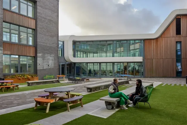Students are sitting on the bench in front of the modern building at the Bangor University