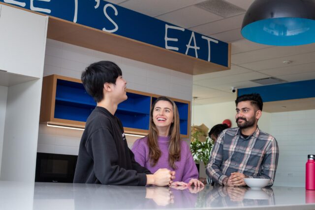 Three students talking in a kitchen