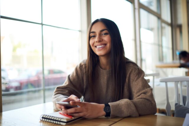 Female sat down with phone and notebook smiling at camera
