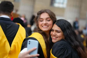 Two smiling graduates in gowns taking a selfie at Dundee graduation ceremony